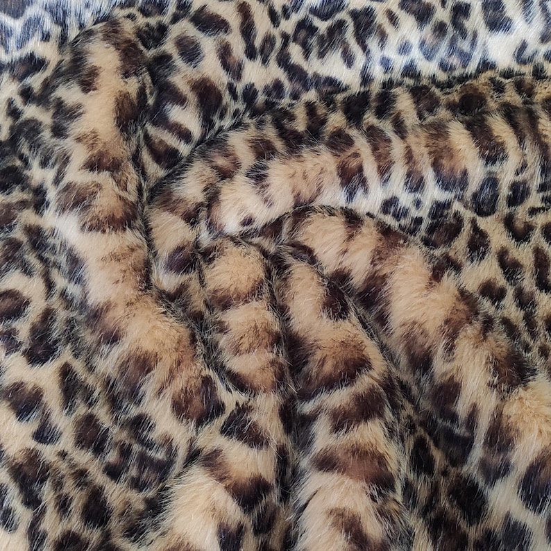 Puede incluir: Primer plano de una tela de piel sint&eacute;tica con estampado de leopardo. La tela presenta una base beige con manchas marrones oscuras y negras, creando un dise&ntilde;o texturizado y animal. El material parece suave y afelpado.