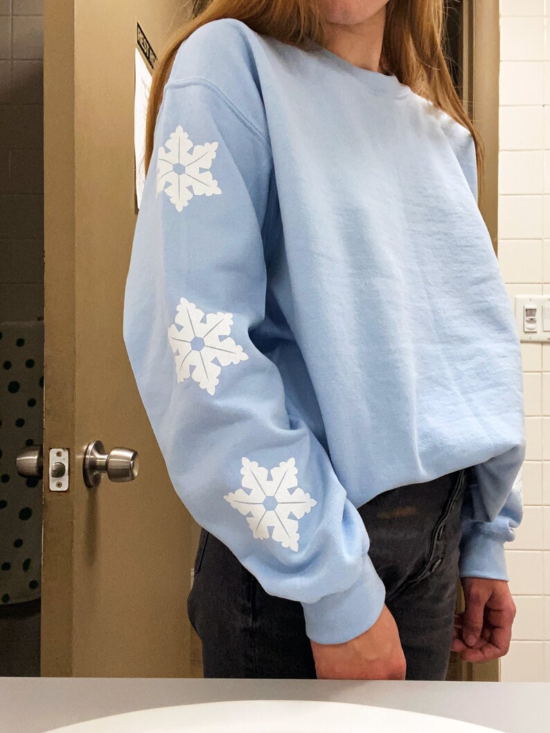 May include: A light blue sweatshirt with white snowflake designs on the sleeves.