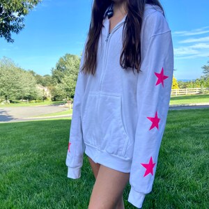 May include: White zip-up hoodie with pink star accents on the sleeves.