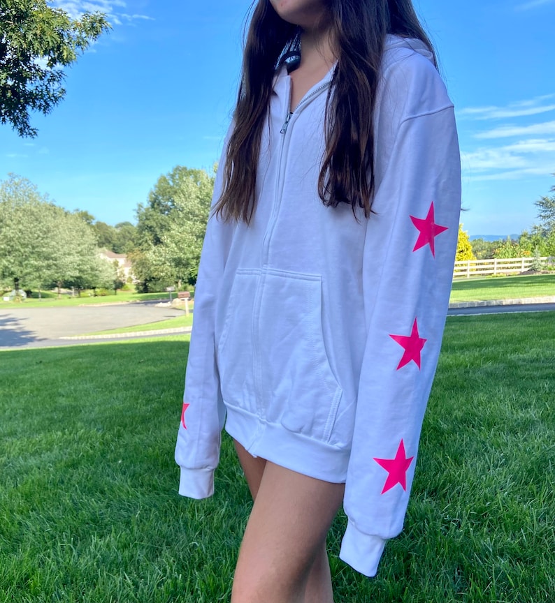 May include: White zip-up hoodie with pink star accents on the sleeves.
