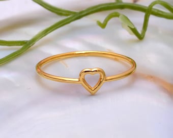 May include: A thin, polished gold-tone ring featuring a small, centered open heart design. The band is smooth and circular, showcasing a bright metallic finish that reflects light across its surface, creating a simple and elegant jewelry piece.