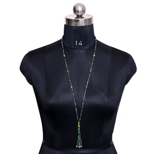 May include: A long green beaded necklace with a tassel at the end. The necklace features a variety of colored beads, including green, blue, red, and orange.