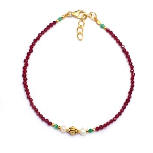 May include: A delicate gold bracelet with red and green gemstone beads and a gold charm with two white pearls.