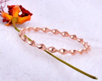 May include: A rose gold twisted bangle bracelet. The bracelet is made of a single piece of metal that is twisted into a spiral shape.