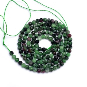 May include: A strand of green and pink faceted gemstone beads. The beads are round and have a smooth, polished finish.