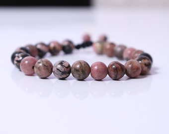 May include: A pink and black gemstone bracelet with a knotted cord closure.