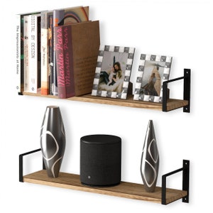 Two rustic shelves burnt holding a variety of books, family frames and stylish vases. These shelves are made of wood and supported by black metal brackets that attach to the wall, giving them a modern and somewhat industrial look.