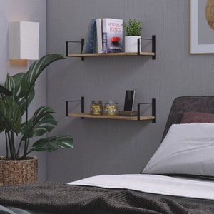 Two bedroom shelves burnt holding books, a mobile phone and other stylish items. These rustic shelves are made of wood and supported by black metal brackets that attach to the wall, giving them a modern and somewhat industrial look.