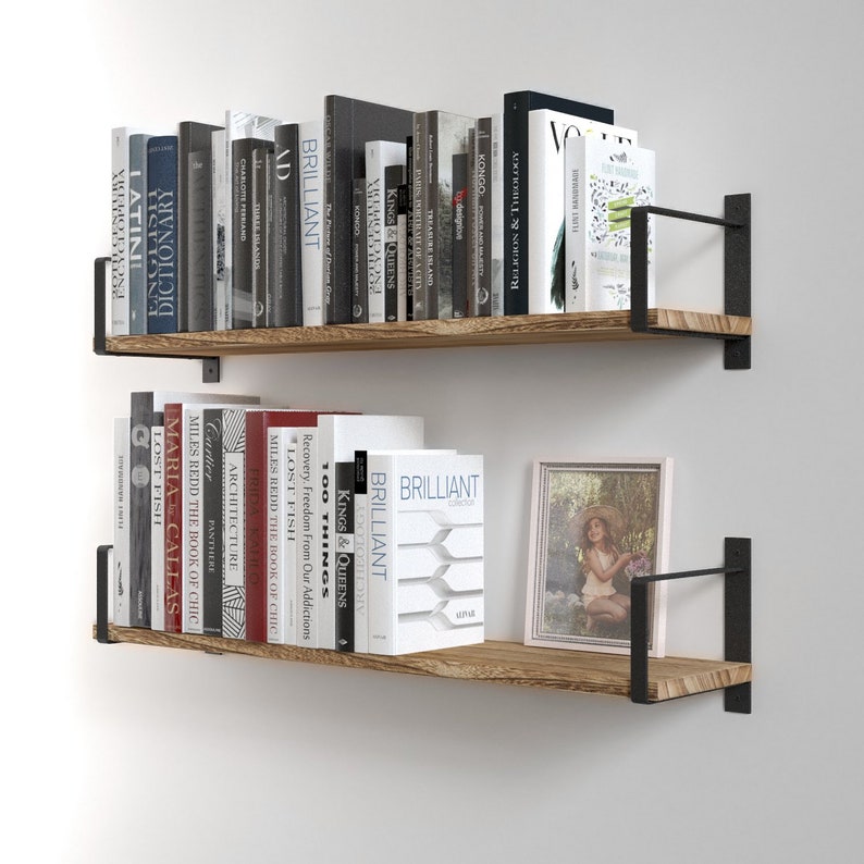 Two wall mounted shelves burnt holding a variety of books. These shelves are made of wood and supported by black metal brackets that attach to the wall, giving them a modern and somewhat industrial look.