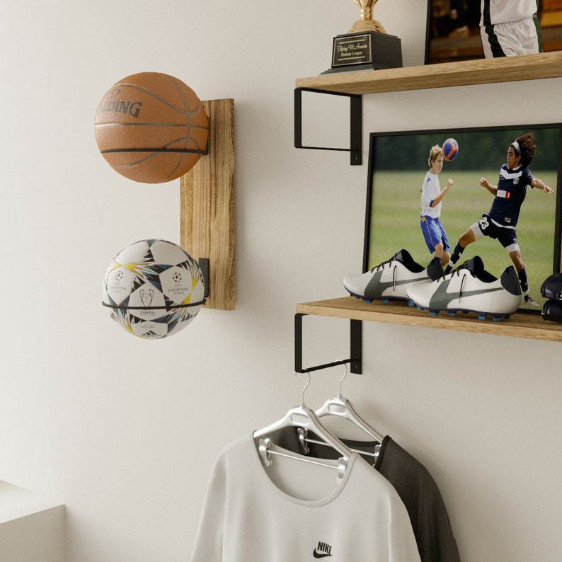 Two book shelves for kids room holding sport items, football shoes and a sportive picture frame. Wood shelves are made of wood and supported by black metal brackets that attach to the wall, giving them a modern and somewhat industrial look.