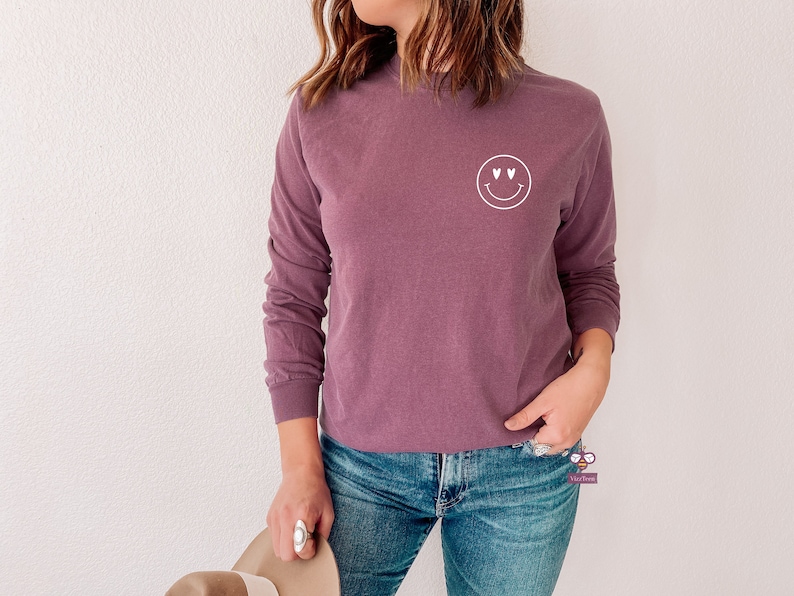 May include: A long-sleeved, mauve colored t-shirt with a white smiley face graphic with heart eyes.