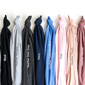 May include: A collection of folded t-shirts in various colors, including white, black, navy, and pink. Each shirt is labeled with its color name, such as "Heather Athletic" and "Heather Maroon". The shirts are displayed against a white background.