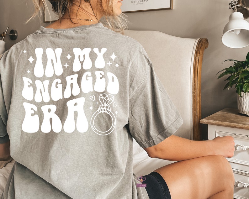 May include: Gray t-shirt with the text "In My Engaged Era" in white retro font with a diamond ring graphic.