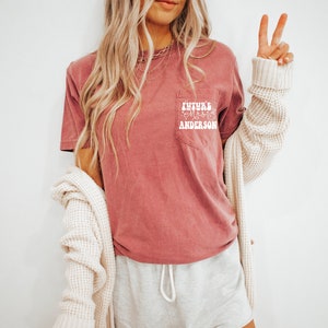 May include: A mauve t-shirt with a white pocket featuring the text "Future Mrs. Anderson" in a retro font.