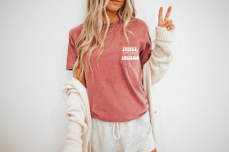 May include: A mauve t-shirt with a white pocket featuring the text "Future Mrs. Anderson" in a retro font.