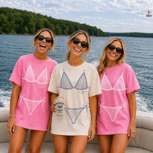 May include: Two pink and one cream short-sleeve t-shirts featuring a white or blue graphic print of a bikini top and bottom. The shirts include the text "Last Hampton 2024" and one person holds a beverage can with "Bachelor Party" printed on it.