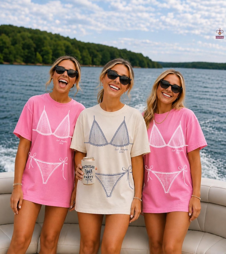 May include: Two pink and one cream short-sleeve t-shirts featuring a white or blue graphic print of a bikini top and bottom. The shirts include the text "Last Hampton 2024" and one person holds a beverage can with "Bachelor Party" printed on it.