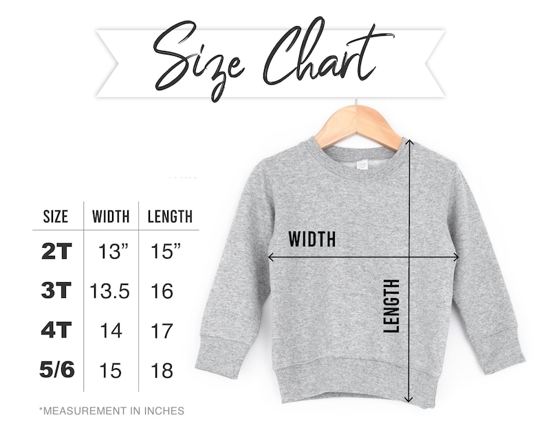 May include: A gray sweatshirt displayed on a wooden hanger, with a size chart showing measurements in inches. The chart lists sizes 2T, 3T, 4T, and 5/6, with corresponding width and length measurements. The text "Size Chart" is written above the sweatshirt.