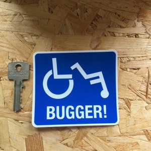 Könnte beinhalten: Blauer quadratischer Aufkleber mit einem weißen Rollstuhlsymbol und dem Text "BUGGER!" in weißen Buchstaben.