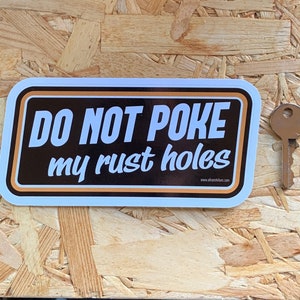 May include: A white sticker with a black background and orange border. The sticker says "DO NOT POKE my rust holes" with a website address at the bottom.