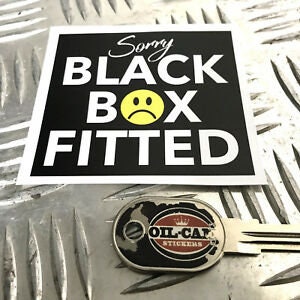 May include: Black and white square sticker with white text that reads "Sorry Black Box Fitted" and a yellow smiley face with a single tear. The sticker is on a gray surface.