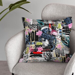 May include: A colourful throw pillow with a black and white tiger print, pink flowers, and text that says "You are Love London Paris" and other words. The pillow is on a grey armchair.