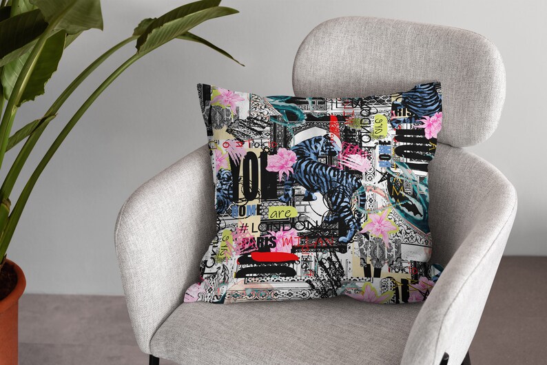 May include: A colourful throw pillow with a black and white tiger print, pink flowers, and text that says "You are Love London Paris" and other words. The pillow is on a grey armchair.