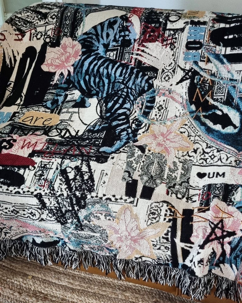 Puede incluir: Una manta de tejido de tapicer&iacute;a con un esquema de color negro, blanco, azul y rosa. La manta presenta un dise&ntilde;o gr&aacute;fico de un tigre, flores y texto. El texto incluye las palabras "are" y "UM".