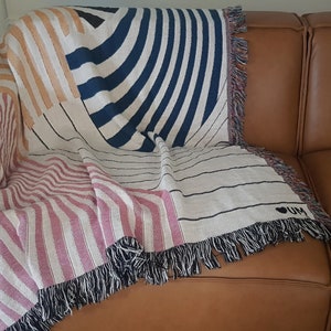May include: A woven throw blanket with a geometric pattern in shades of pink, orange, white, and blue. The blanket has fringe on all sides and features the text "I LOVE" in black.