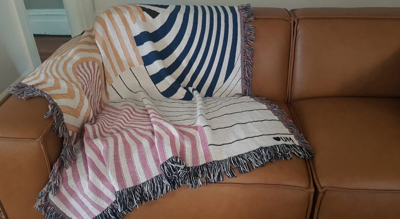 May include: A woven throw blanket with a geometric pattern in shades of pink, orange, white, and blue. The blanket has fringe on all sides and features the text "I LOVE" in black.