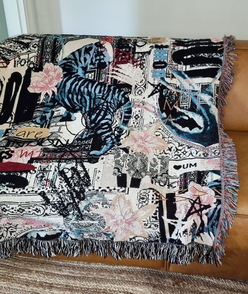 Puede incluir: Una manta de tejido de tapicer&iacute;a con un dise&ntilde;o abstracto en negro, blanco y azul que presenta un tigre, flores y las palabras "are my" y "UM".