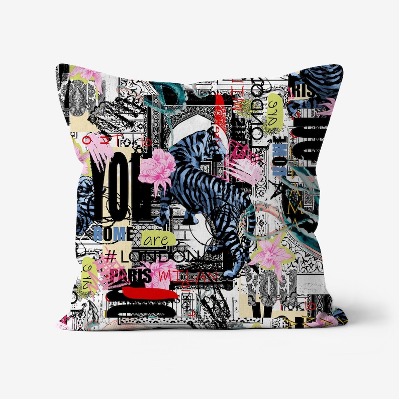 May include: A white cushion with a colourful design featuring a black and blue striped tiger, flowers, and text that says "You are Rome, London, Paris, Tokyo, NYC, LA, Berlin, Madrid, Amsterdam, Sydney, Rome, London, Paris, Tokyo, NYC, LA, Berlin, Madrid, Amsterdam, Sydney".