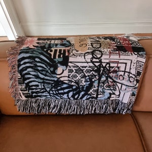 Puede incluir: Una manta tejida con un dise&ntilde;o abstracto colorido que presenta un patr&oacute;n de cebra, l&iacute;neas blancas y negras y las palabras "WILD" y "RIS".
