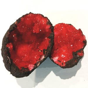 May include: Two red crystal geodes with a dark brown exterior. The crystals are visible inside the geodes.