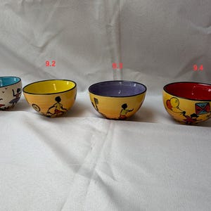 May include: Four brightly coloured ceramic bowls with hand-painted designs. Each bowl has a different interior colour: teal, yellow, purple, and red. The exterior of each bowl is yellow with a painted scene of a person.