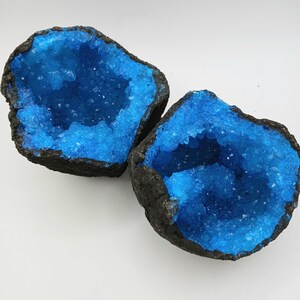 May include: Two blue crystal geodes with black exteriors. The geodes are open and reveal a blue crystal interior.