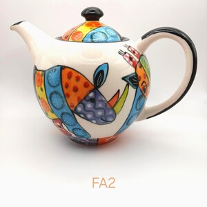 May include: A ceramic teapot with a white base featuring colourful hand-painted patterns of a rhinoceros and abstract shapes in orange, blue, yellow, and purple. The teapot has a black handle, a black lid knob, and the text FA2 printed below it.