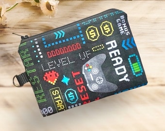 May include: Black zippered pouch with a pixelated video game theme. The design includes a game controller, dollar signs, and the words "READY", "LEVEL UP", and "BONUS GAME". The pouch has a small loop on the side.