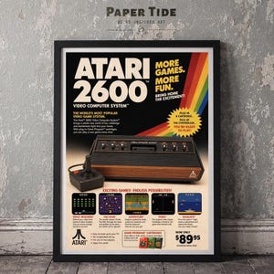 May include: A framed vintage advertisement poster for the Atari 2600 video computer system. The poster features the console, a joystick controller, and screenshots of games like Space Invaders, Pac-Man, Adventure, Pong, and Seaquest with text.