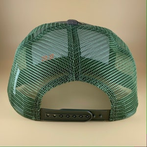May include: Green and black mesh trucker hat with an adjustable plastic strap at the back.