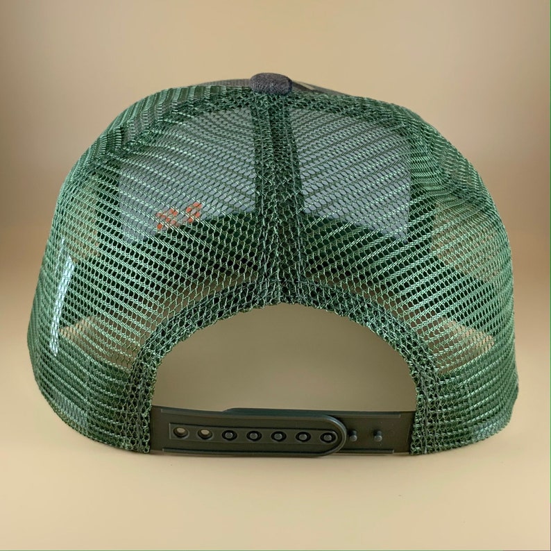 May include: Green and black mesh trucker hat with an adjustable plastic strap at the back.