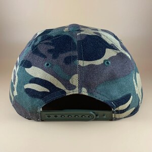 May include: A camouflage baseball cap with a green adjustable strap at the back.