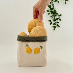 Op de afbeelding: Een witte canvas tas met een groene rand en een citroendesign. De tas is gevuld met ronde broodjes.