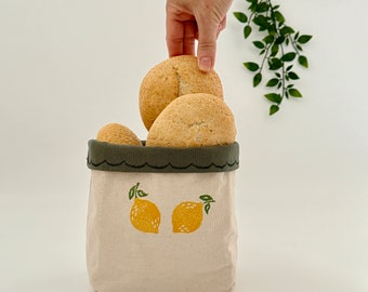 Op de afbeelding: Een witte canvas tas met een groene rand en een citroendesign. De tas is gevuld met ronde broodjes.