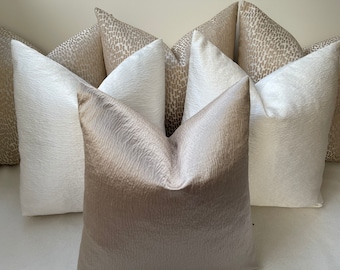 May include: A selection of decorative cushions in neutral colours. The cushions display textured fabrics in ivory, beige, and light taupe. Some have a subtle pattern, while others are plain, creating a layered and elegant aesthetic for home decor.