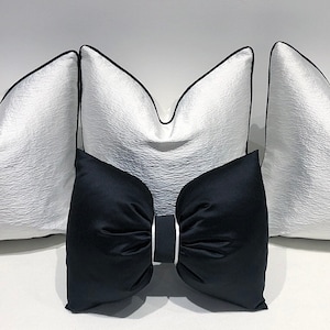 May include: Three white throw pillows with black trim, one black throw pillow with a large bow in the center.