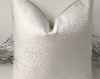 May include: A white throw pillow with a subtle textured pattern and a gray trim. The pillow is made of a soft, luxurious fabric.