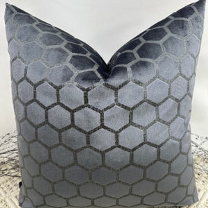 Puede incluir: Una almohada de terciopelo gris con un patrón de panal negro.
