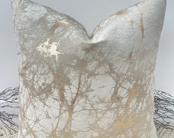 May include: A decorative throw pillow with a white background and a gold abstract pattern. The pattern resembles branches or veins.