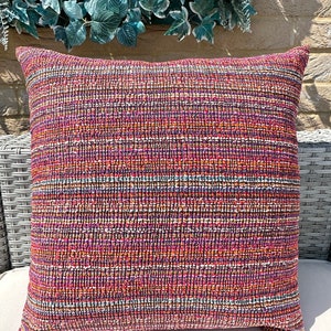 May include: Multicoloured striped throw pillow with a textured woven fabric. The pillow is a deep red colour with orange, purple, and blue stripes.